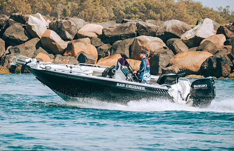 Man standing up, driving XSR Series boat with rocks in the background